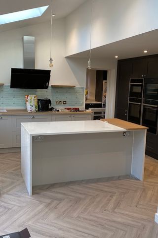 A white and grey kitchen renovation with a white island set ontop of a herringbone flooring.
