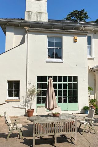The rear of the house, with green french doors leading onto a patio and a dining area.