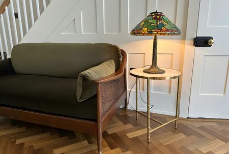A traditional seating room with woodern herringbone flooring with a green 2 seater sofa and table lamp next to it.