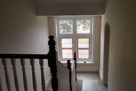 Looking down the stairs to a landing area which has been fully decorated and the stained glass window repaired and the frame replaced with a white sash.