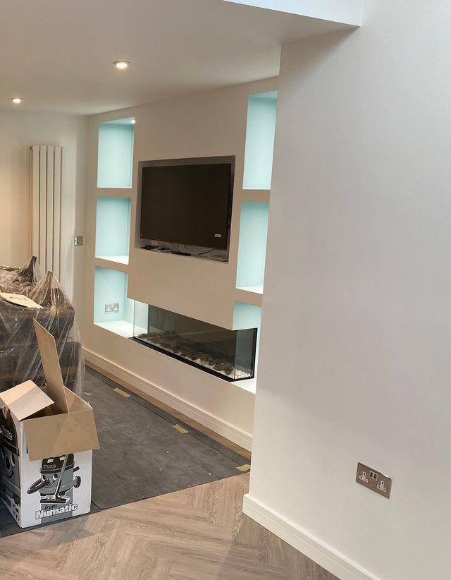 A tv media wall with modern white cubicles and a fish tank below the wall mounted tv.