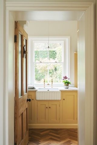 A kitchen with a belfast sink set below a sash window, yellow cabinets, and marble worktops.